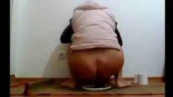 Tanned female ass pooping in a plastic bowl